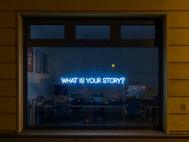 A window with a blue neon sign that says "What is your story?"