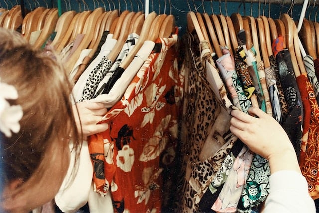 Someone searching through a closet of colorful printed shirts.