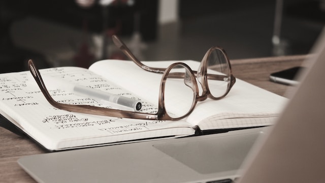 Glasses on top of an open notebook with notes in it and a pen.